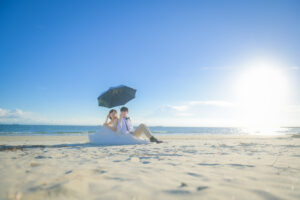 常滑りんくうビーチで洋装ウェディングフォト　砂浜に座り相合傘をする新郎新婦　愛知前撮り